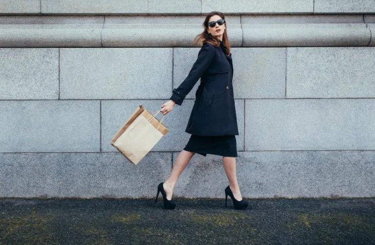 Mujer elegante con gafas de sol caminando con una bolsa de compras