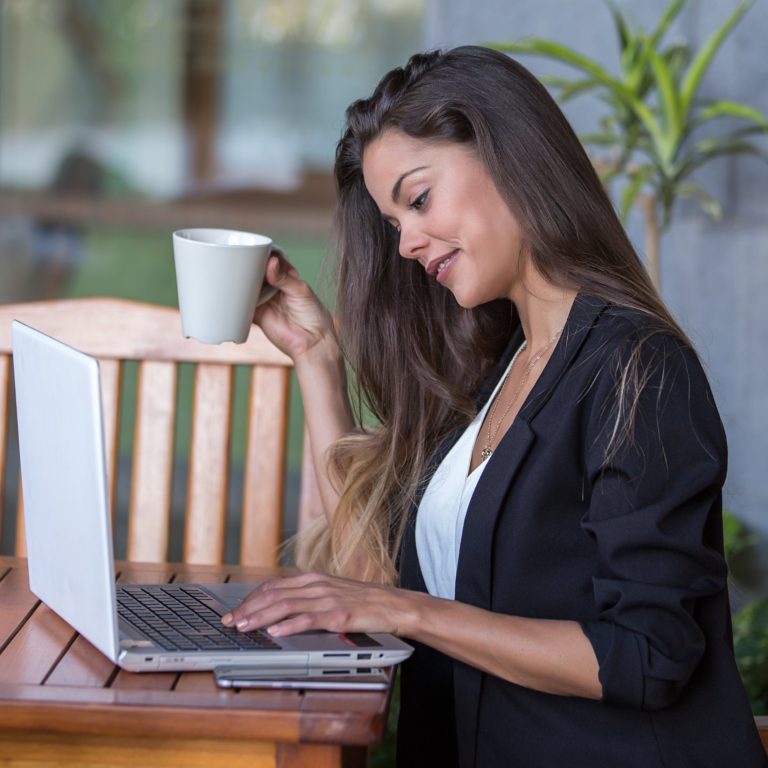Mujer con blazer negro trabajando en su laptop junto a una taza de café