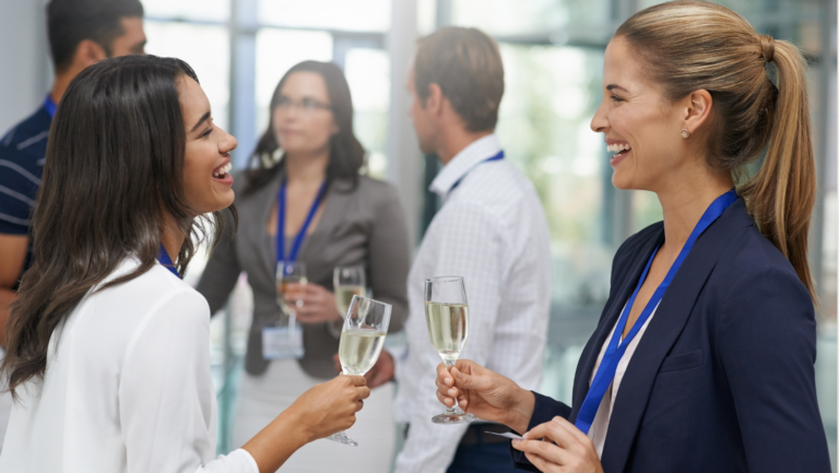 Dos profesionales conversan con copas en un evento de networking, practicando la etiqueta de negocios
